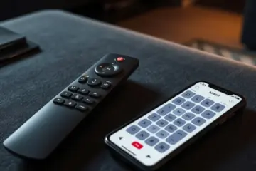 alt_text: A modern IPTV remote and a smartphone displaying a button mapping app, set on a dark surface in a contemporary living room.