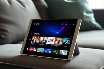alt_text: A sleek tablet on a dark surface displays a vibrant IPTV app with live TV channels in a cozy living room setting.