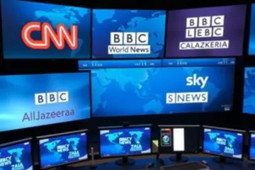alt_text: A high-tech media control room with large screens displaying major international news channel logos and a dynamic world map.
